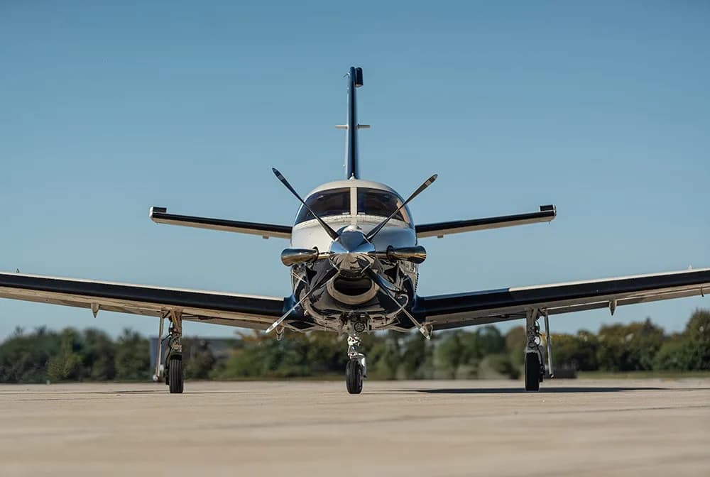 A white, blue, and gold painted turboprop aircraft (N220MA) parked on an airfield, viewed head-on.