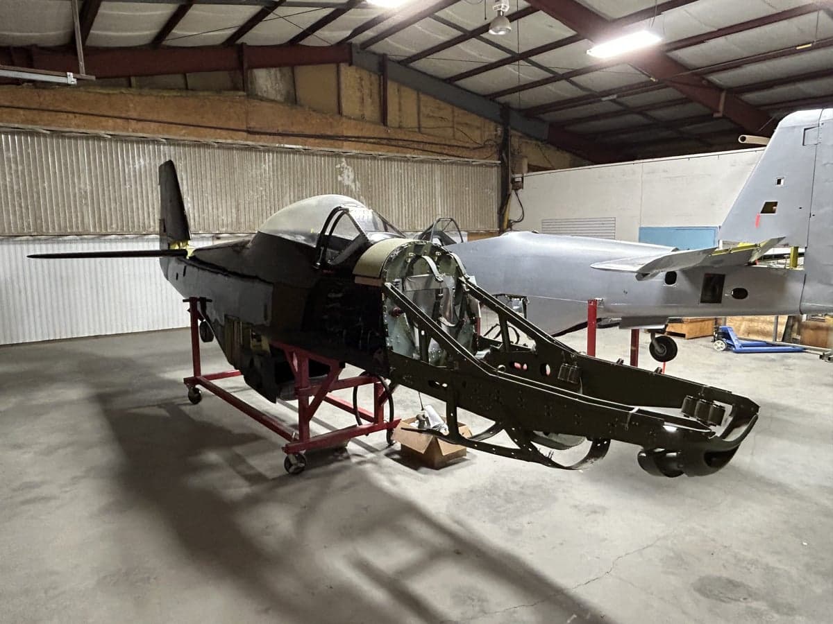 An aircraft fuselage is shown in a hangar, undergoing restoration.