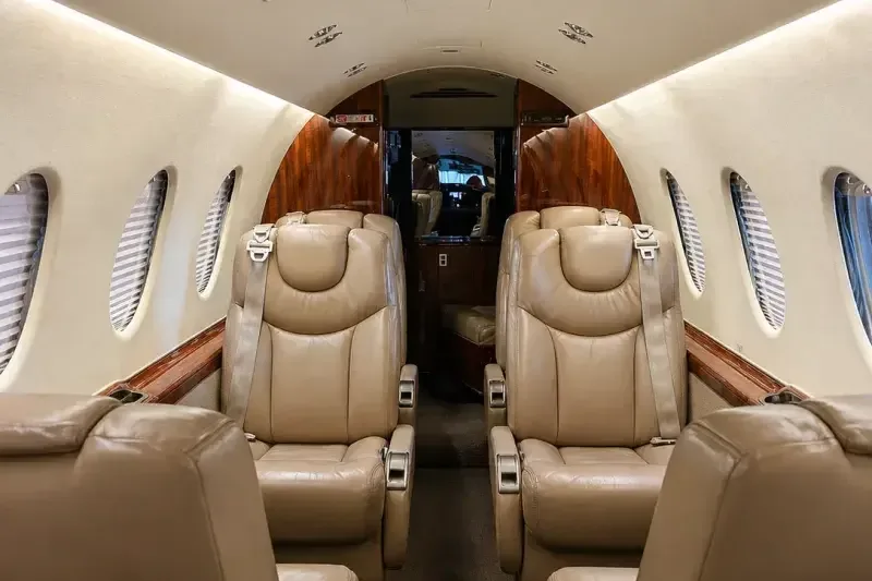 The aircraft's interior cabin shows rows of beige leather seats and wood paneling, looking towards the rear.