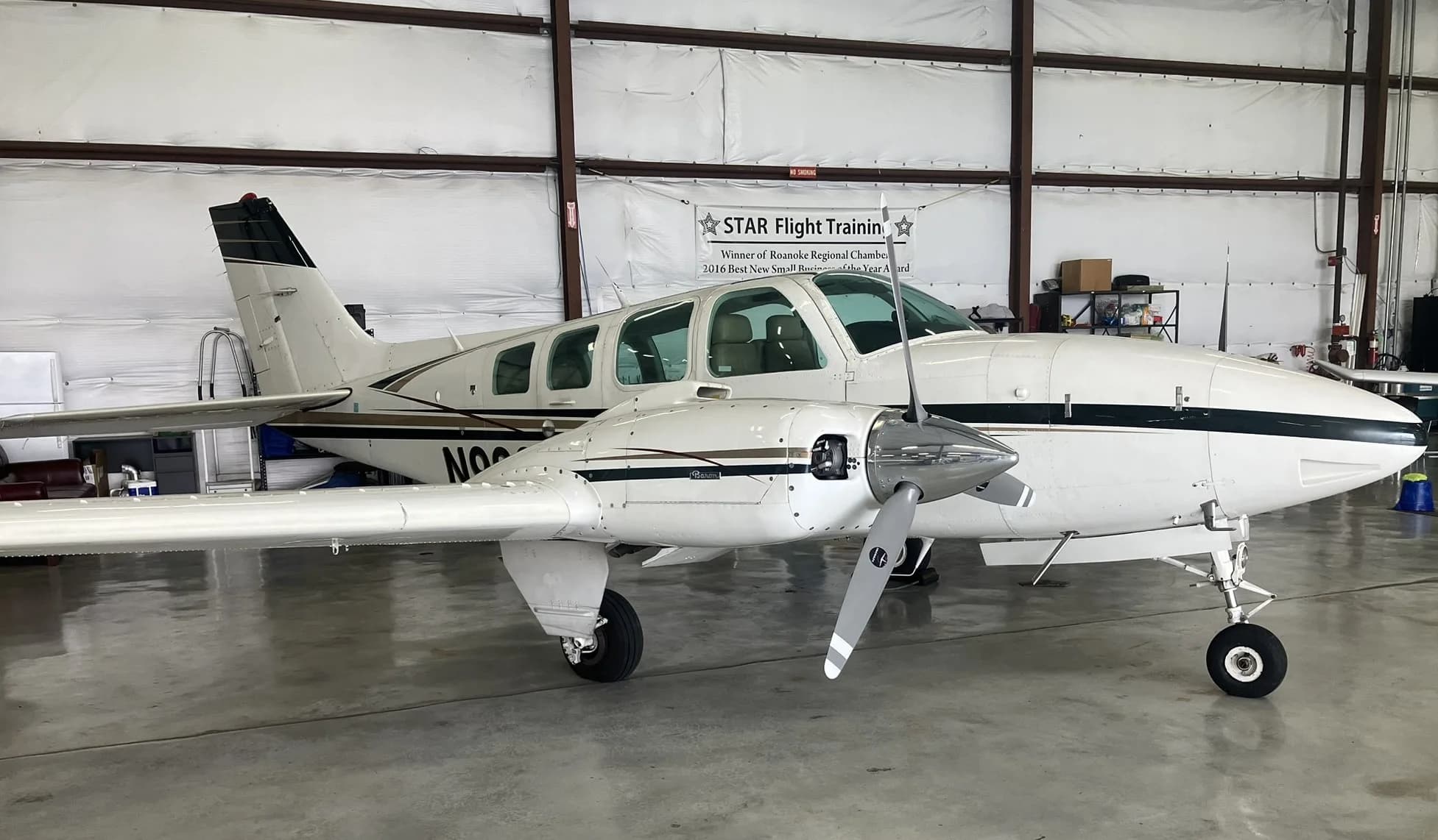 A white twin-engine Beechcraft Baron aircraft with dark stripes is parked inside a hangar.