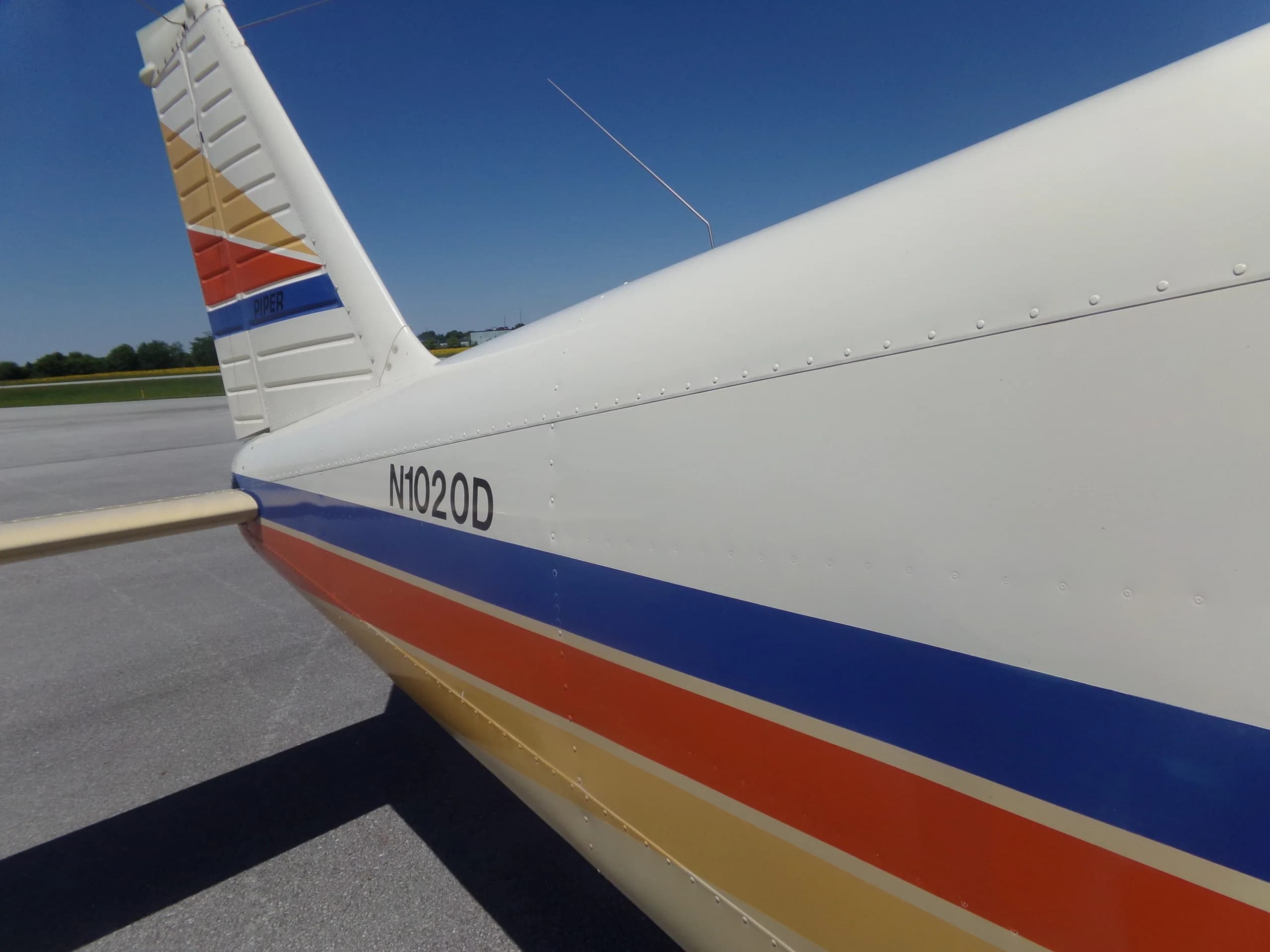 A close-up of the N-number "N1020D" on the white fuselage of a Piper aircraft, with blue and orange stripes.