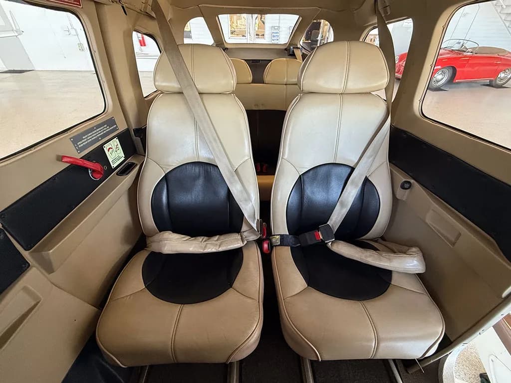 The tan and black leather front seats of the aircraft cabin, with seatbelts fastened.