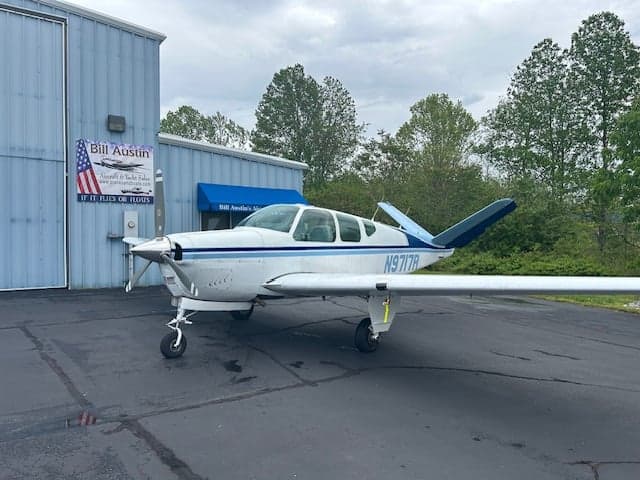 A white and blue Beechcraft Bonanza parked in front of a building.