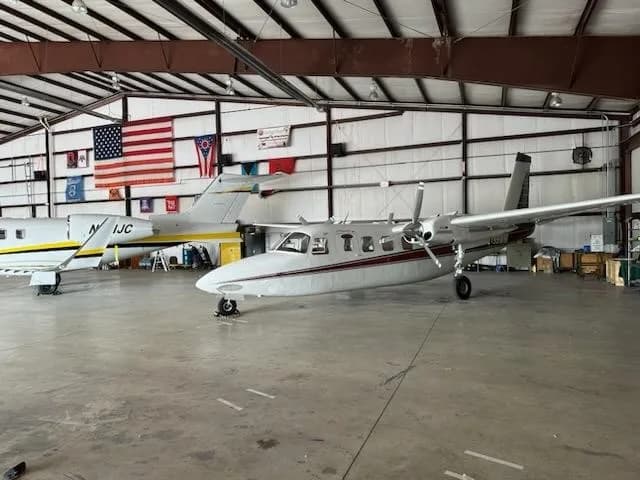 A white and red Aero Commander 680FL twin-engine aircraft, registration N199WM, parked in a hangar next to another aircraft.