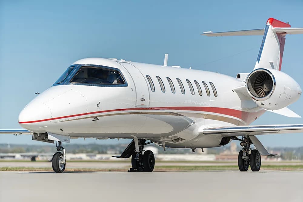 A white private jet with red and gold stripes on the tarmac, viewed from the front-right.