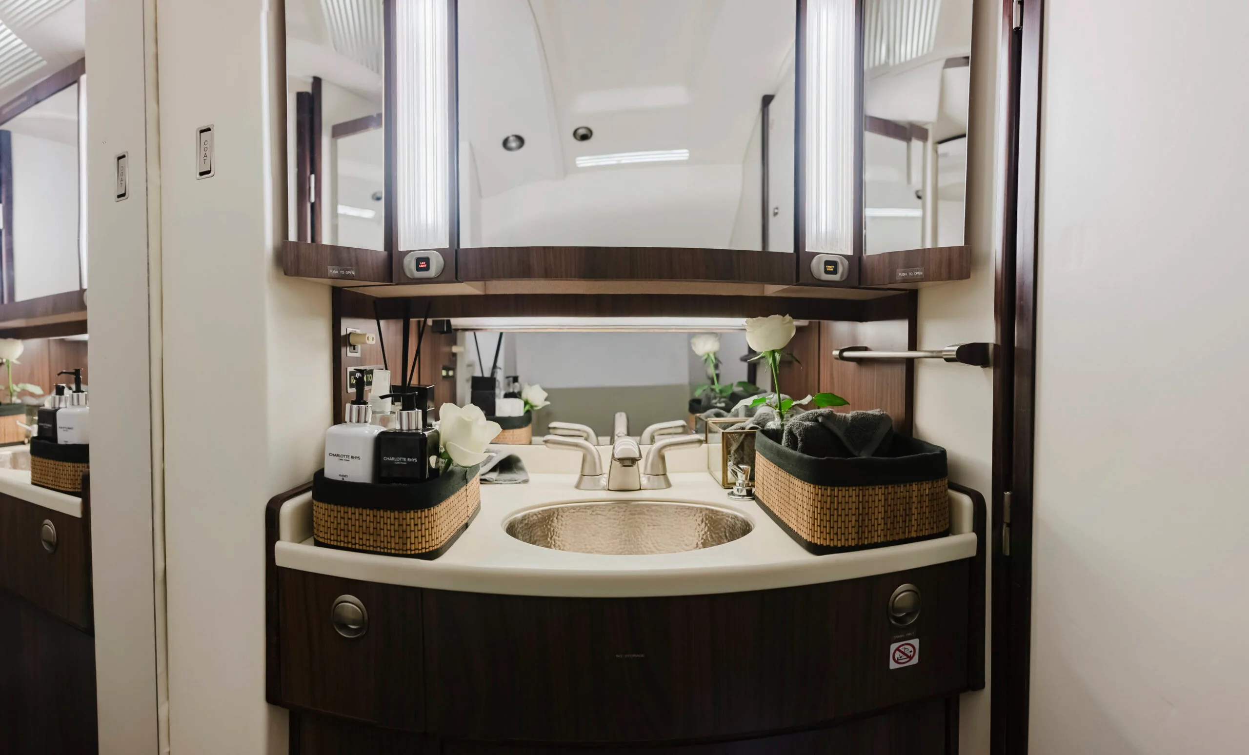 A well-appointed aircraft lavatory sink with a copper basin, mirrors, and white roses.