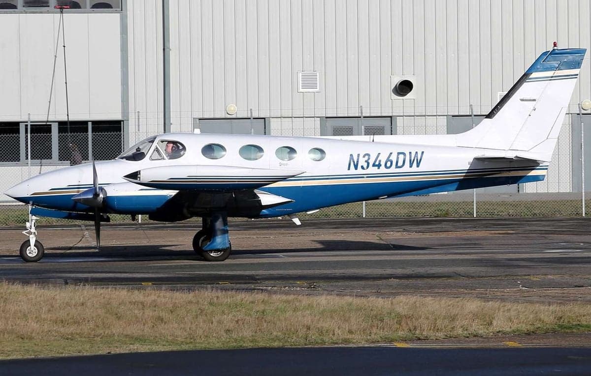 A Cessna 414 Chancellor aircraft on the tarmac with a white and blue paint scheme, side view.
