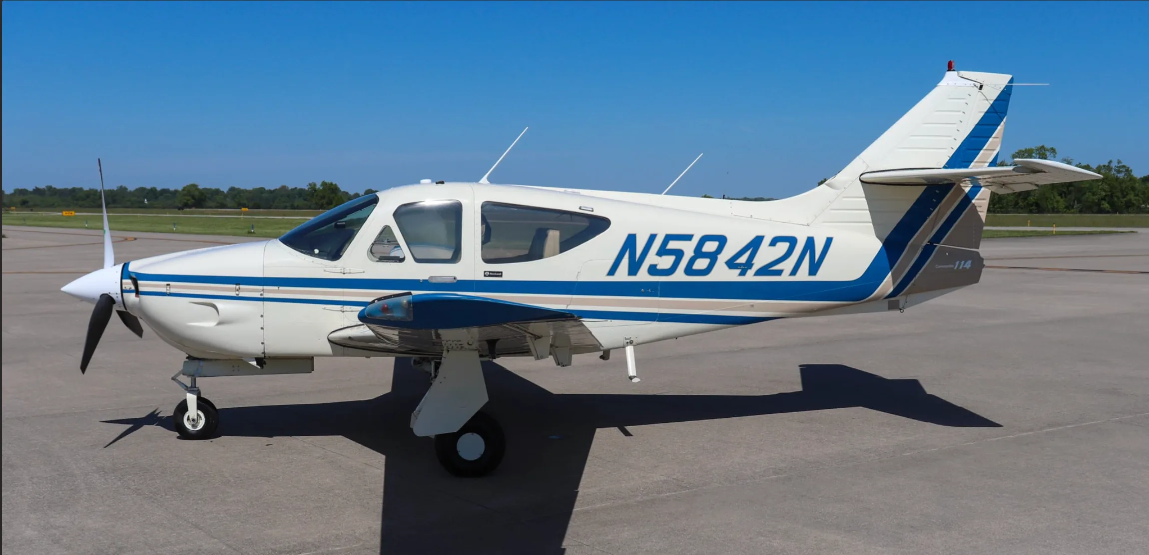Side view of a white single-engine propeller aircraft with blue and tan stripes, registration N5842N, parked on an airfield.