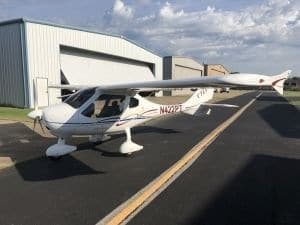 A white single-engine light sport aircraft, N422PT, is parked on an asphalt ramp in front of a hangar under a partly cloudy sky.