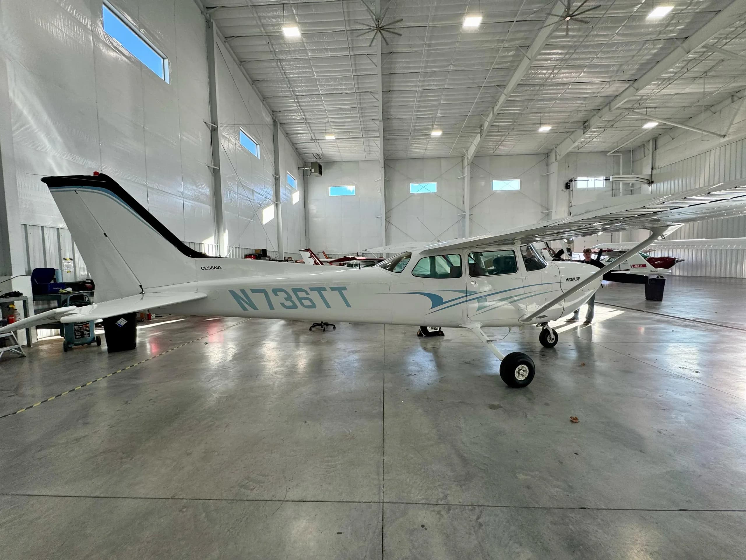 A white Cessna 172 Hawk XP aircraft with blue stripes and registration N736TT is parked inside a hangar.