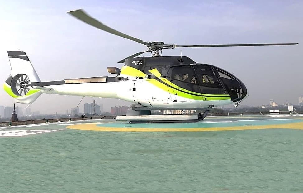 A white and green Airbus helicopter sits on a helipad.