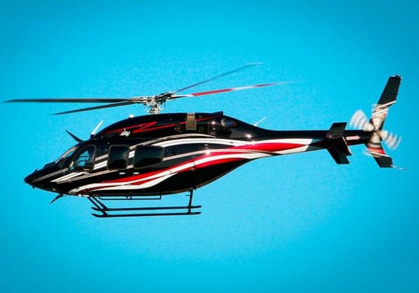 A black and white helicopter with red accents flies against a blue sky.