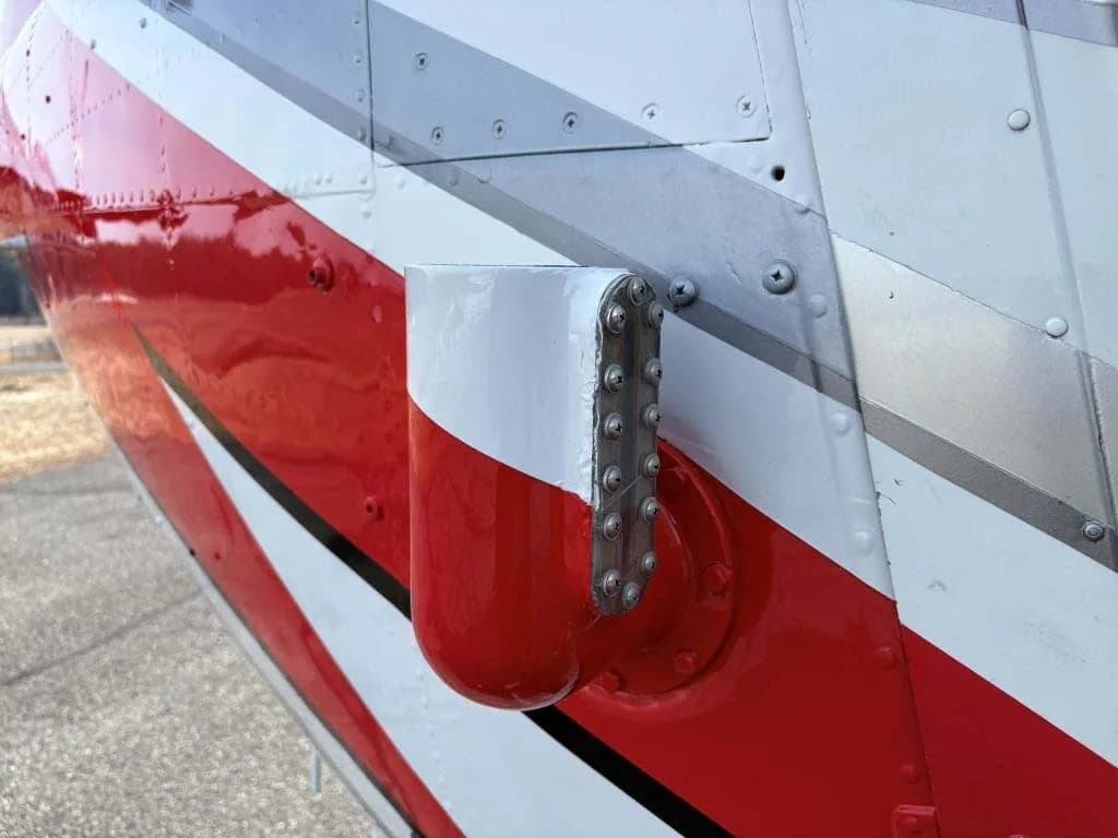 A close-up of a red, white, and black painted helicopter fuselage showing a small external component.