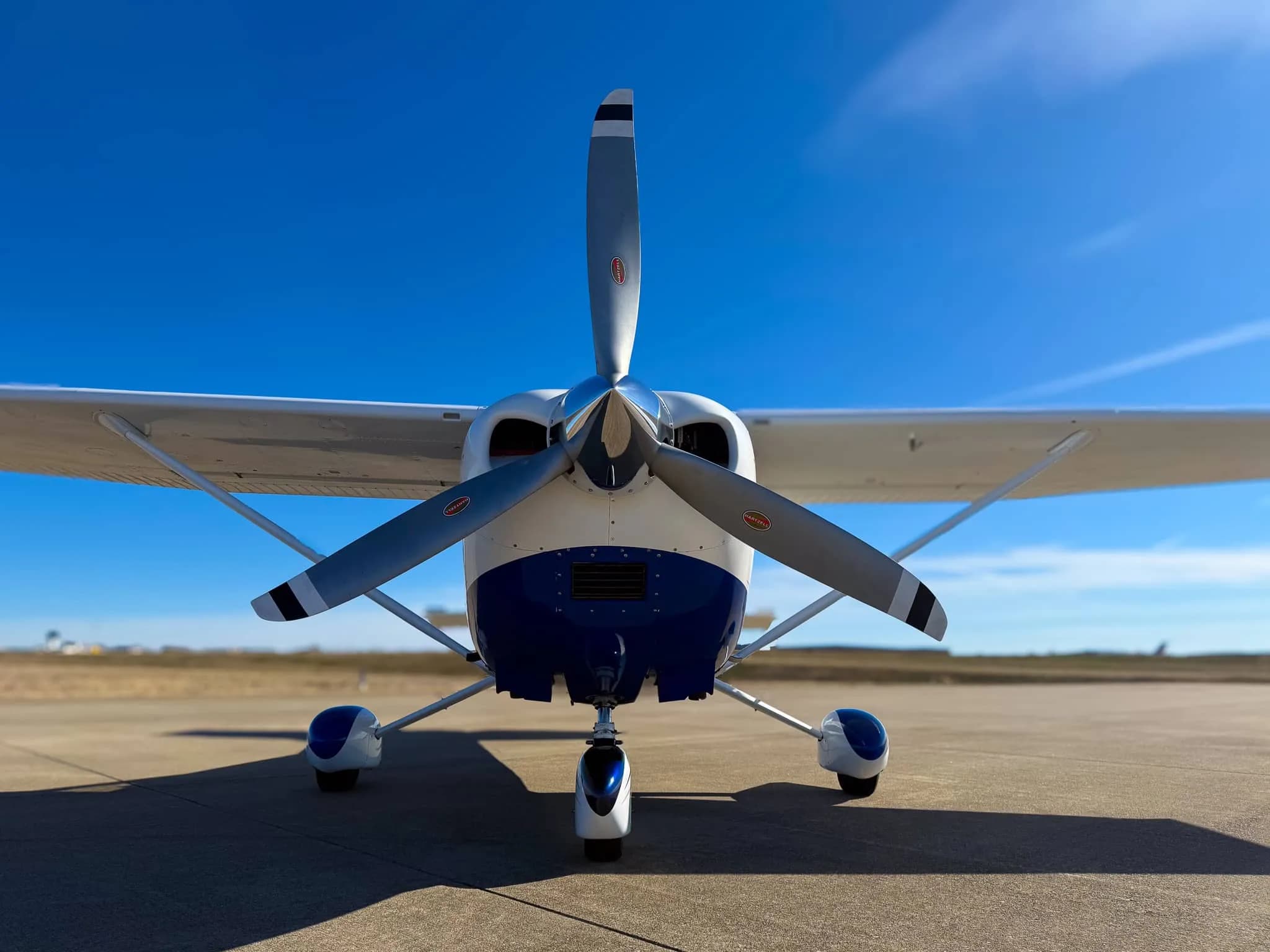 A head-on view of the propeller and nose of a white and blue Cessna 182 Skylane (N2151X).
