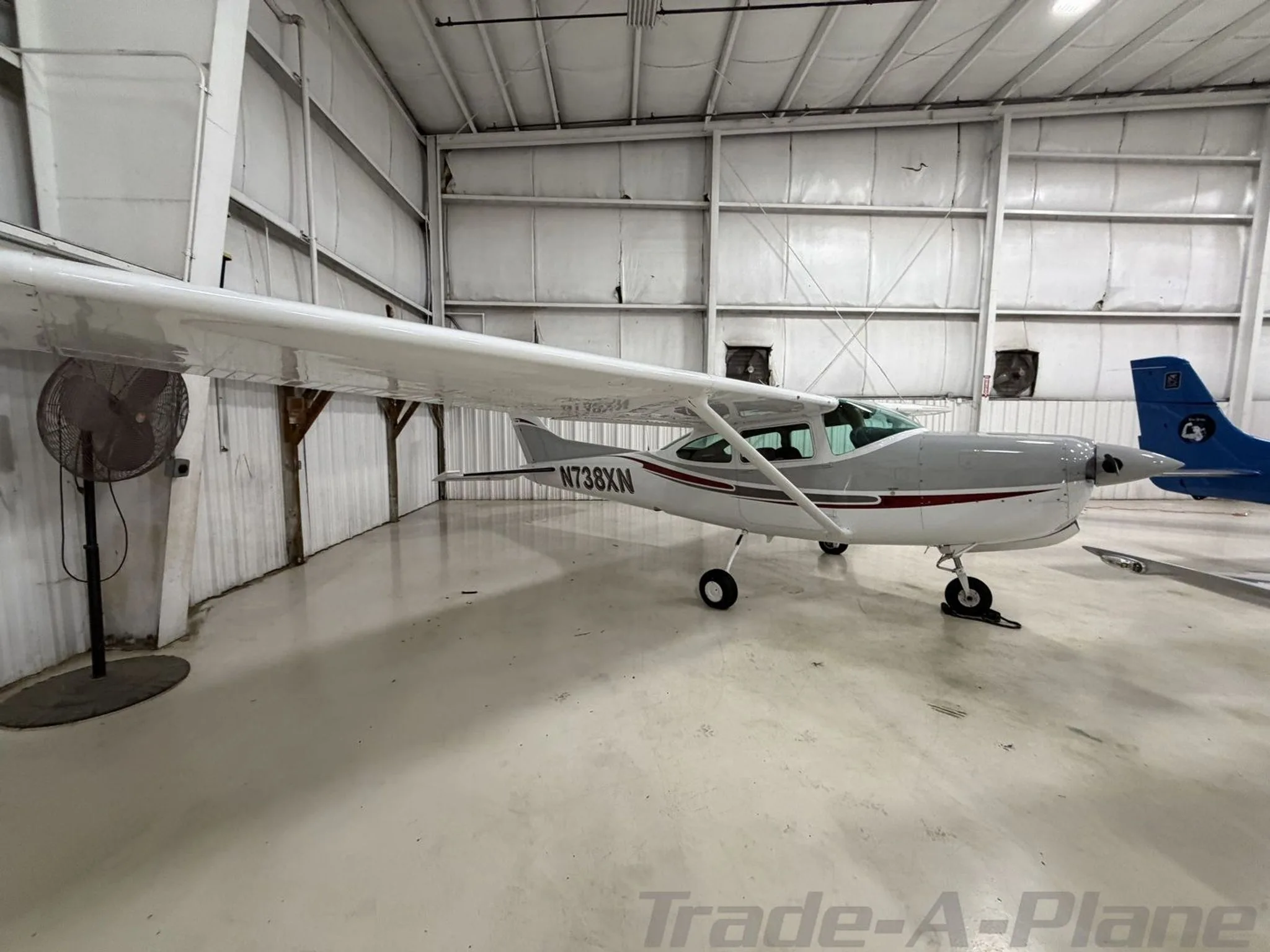 A white and grey Cessna 182 aircraft with red stripes, registration N738XN, parked inside a hangar.