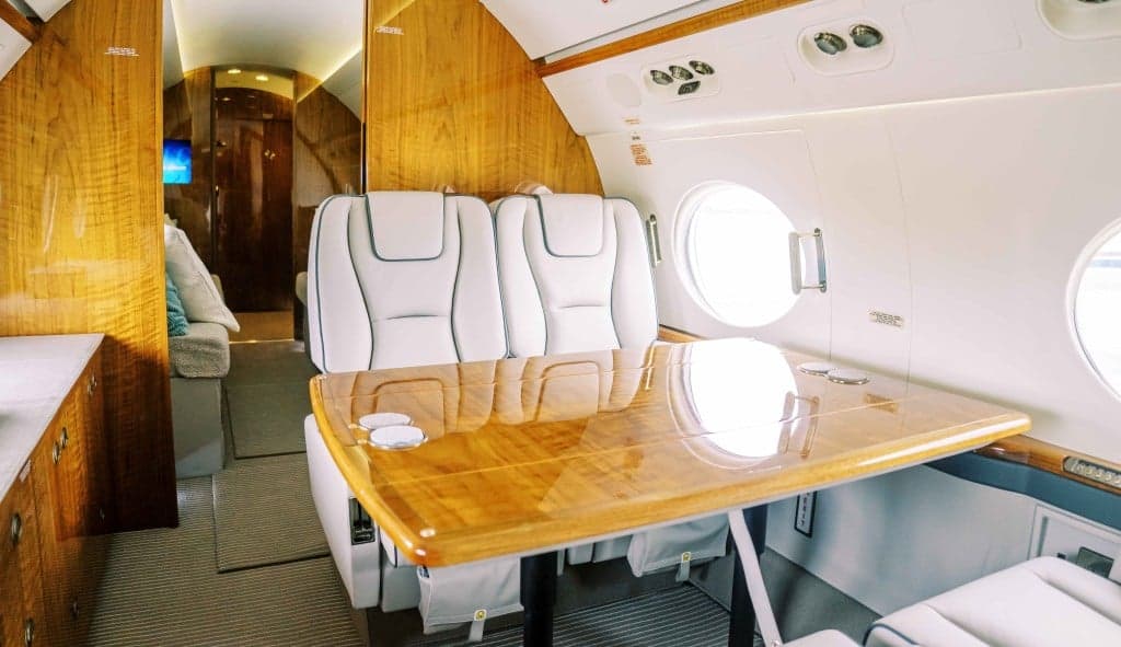 The aircraft's interior features white leather seats and wood trim.