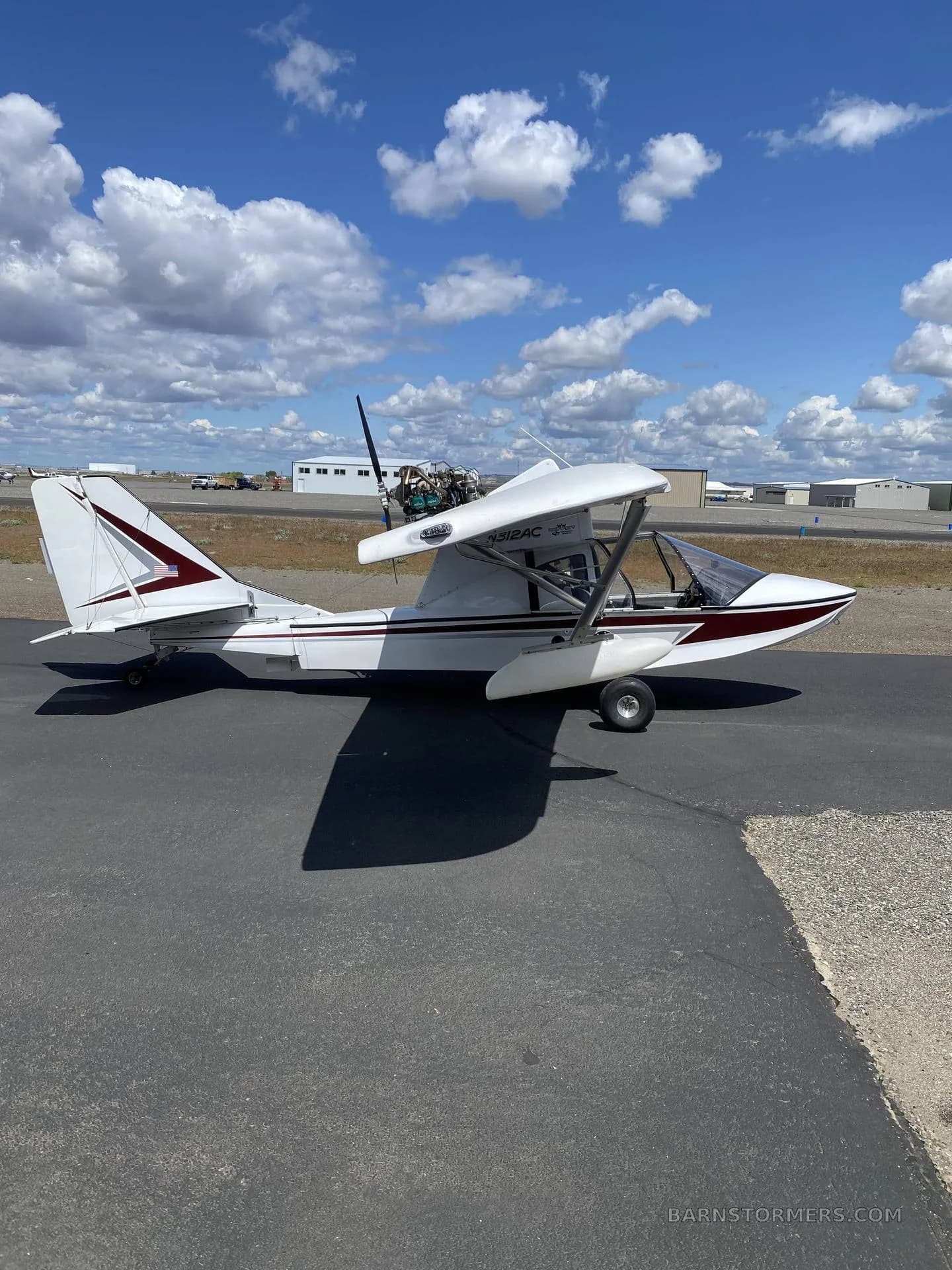 A white and maroon Searey amphibian aircraft with registration N312AC is parked on an asphalt ramp under a partly cloudy sky.