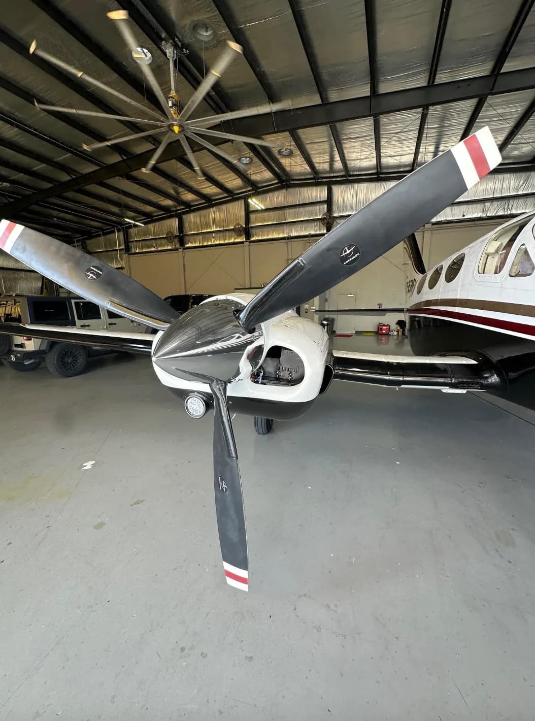 Close-up view of the front propeller and engine cowling of the twin-engine aircraft, N755BC, inside a hangar.