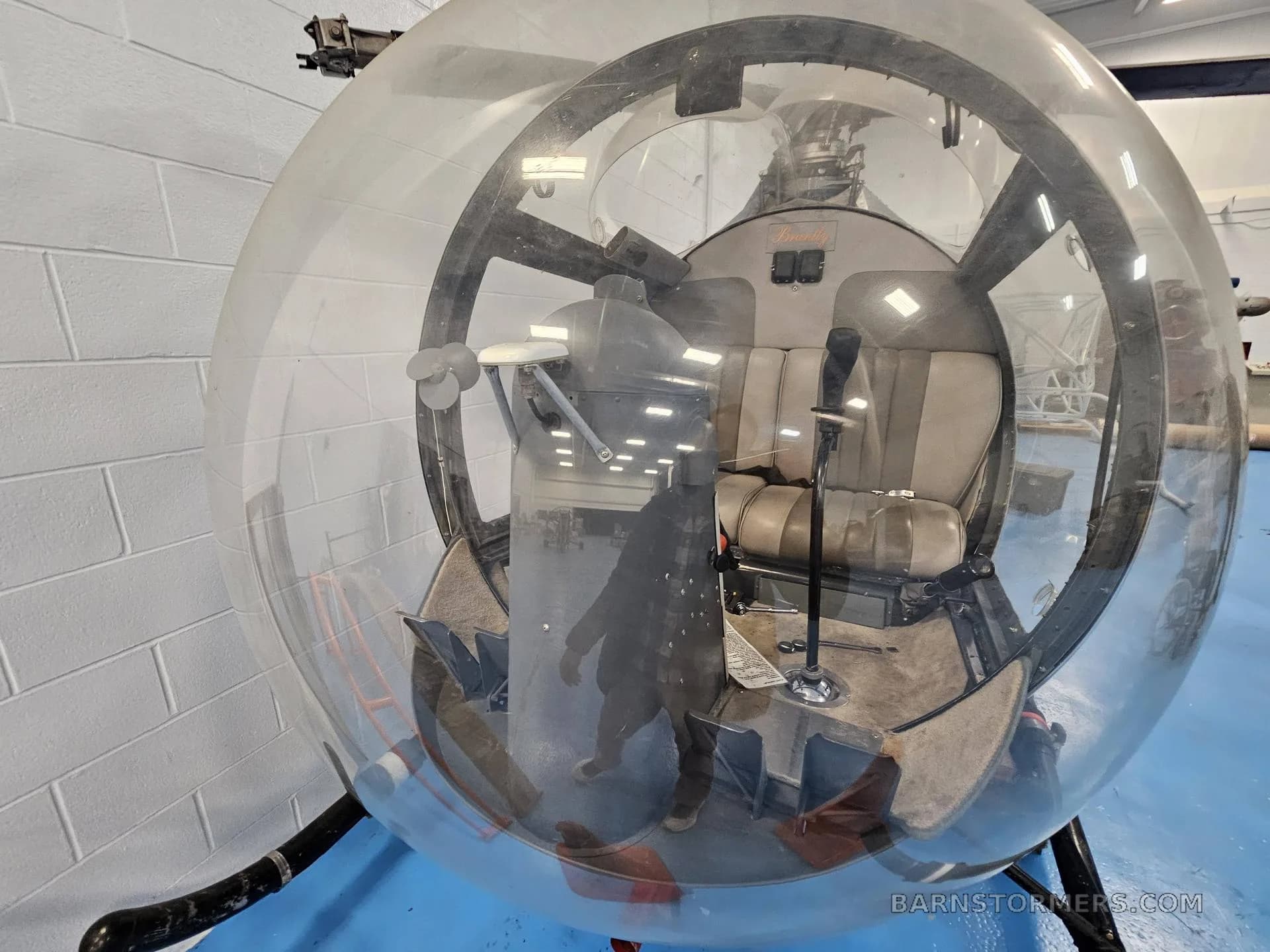 A view into the clear bubble canopy of a helicopter, showing the two-tone grey seats and some controls.