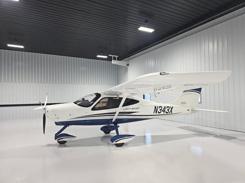 A white and blue Tecnam P2008 Light Sport aircraft (N343X) is parked inside a clean hangar, viewed from the front-left.