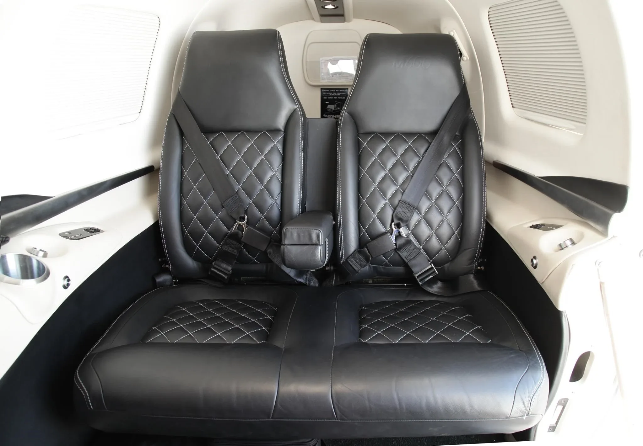 Two black leather passenger seats with diamond stitching and seatbelts in the aircraft cabin.