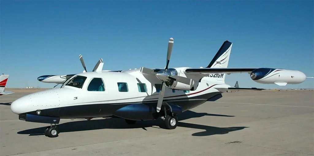 A white and blue twin-engine turboprop aircraft, registration N321GM, parked on an airfield under a clear blue sky.