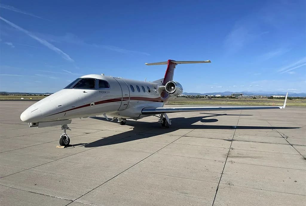 A white and red Embraer Phenom 300 private jet parked on an airport tarmac.