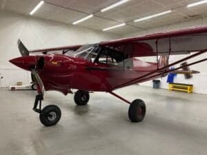 A red Cubcrafters aircraft is parked inside a hangar.