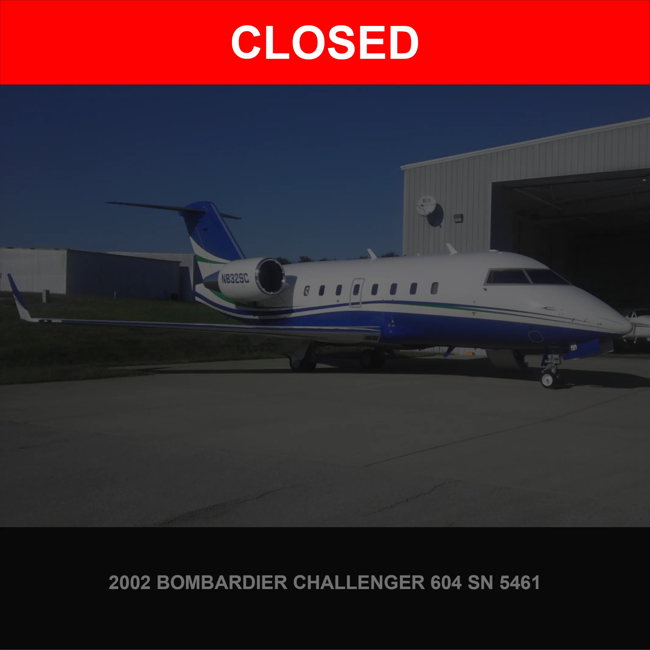 A white and blue Bombardier Challenger 604 business jet, registration N832SC, is parked on an tarmac next to a hangar.