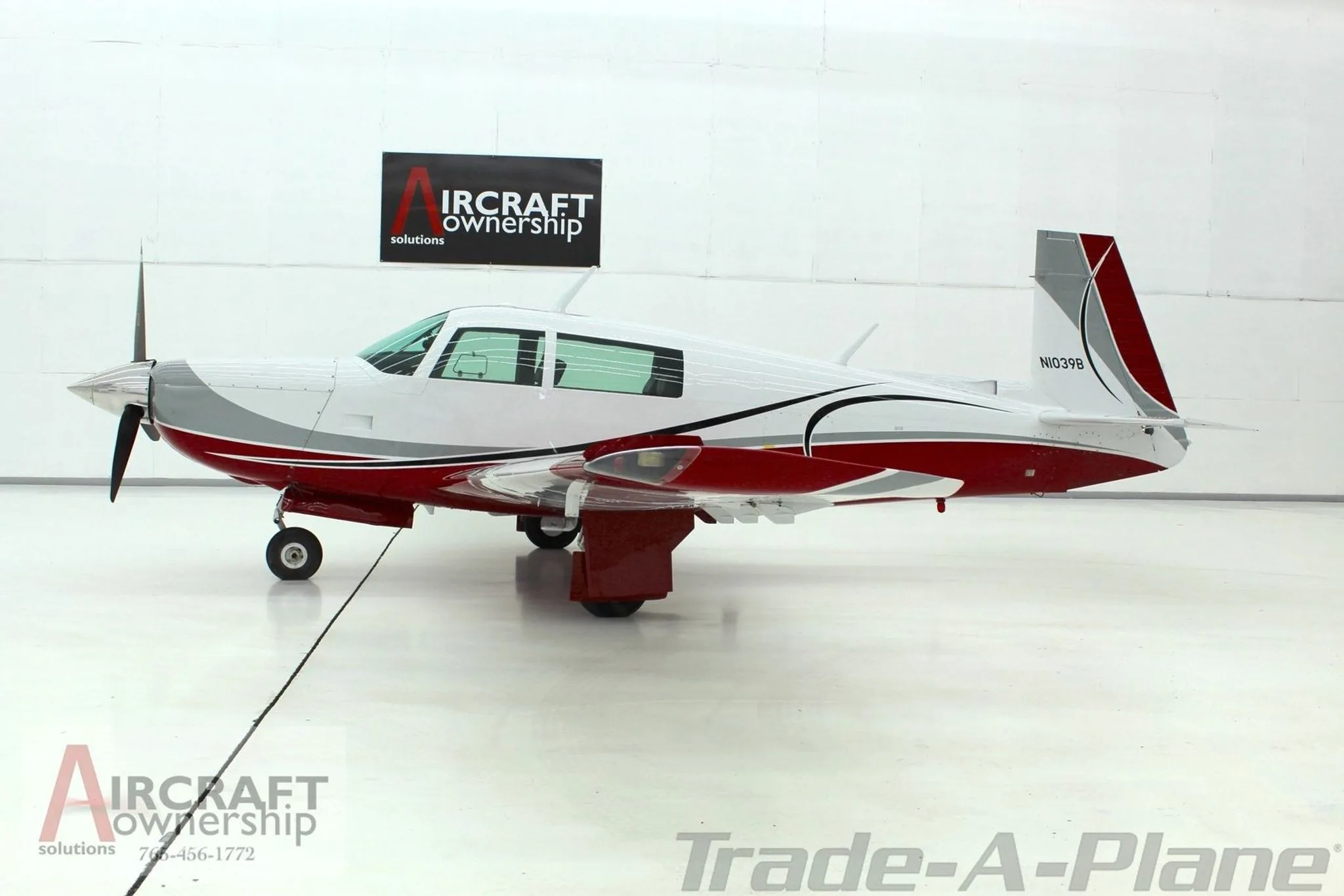 A Mooney aircraft, registration N1039B, in red, white, and grey paint, parked in a hangar.