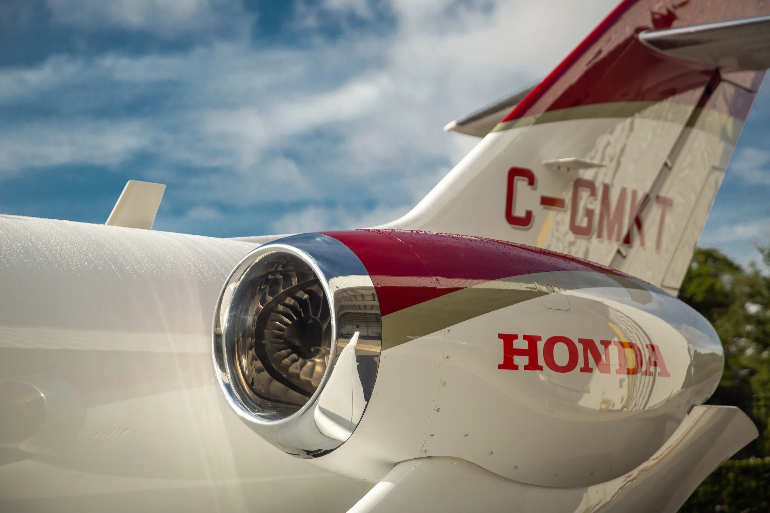 A close-up of the engine and tail of a red and white HondaJet, showing the registration C-GMKT.