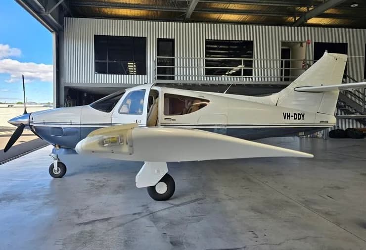 A white and blue aircraft with tail number VH-DDY is parked in a hangar.