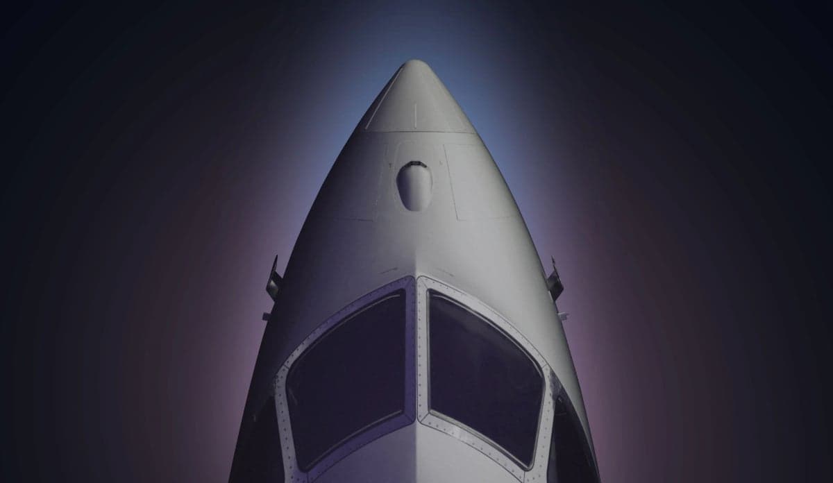 A dramatic, low-angle close-up of the nose and cockpit windows of a silver business jet against a dark, gradient background.