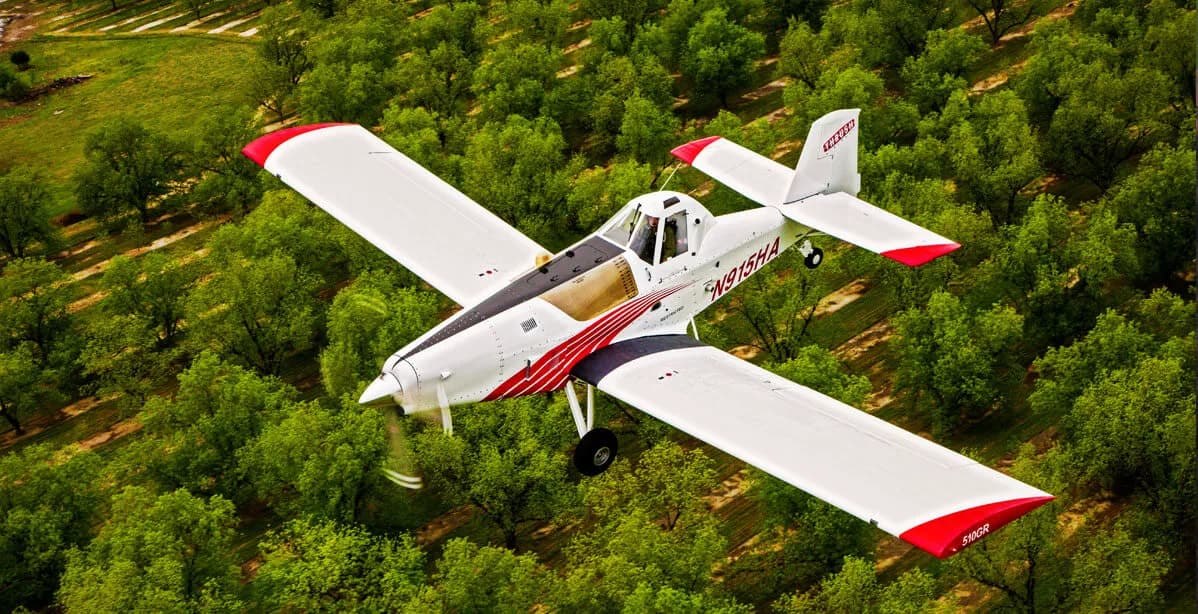 Aerial view of a white and red Air Tractor crop duster flying over trees.