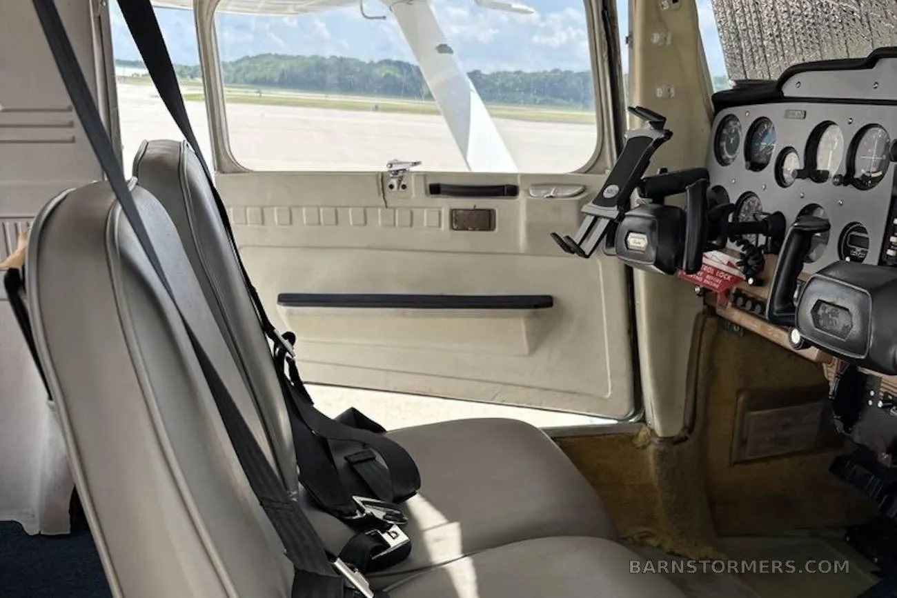 View from the pilot's seat showing the instrument panel, seat, and runway outside the window.