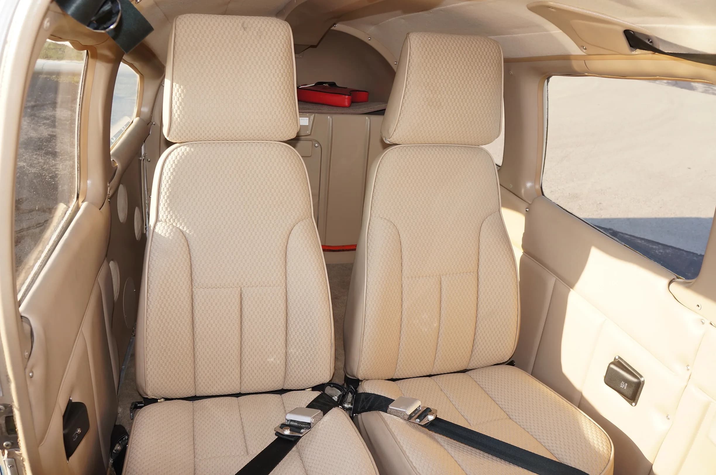 View of the two rear beige seats in the aircraft cabin, with a small red bag visible in the back.