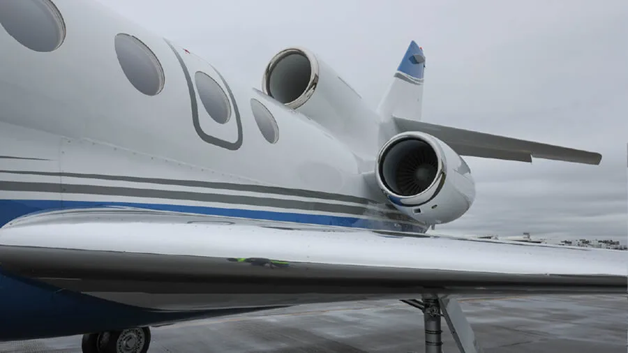 A close-up view of the rear fuselage, engines, and wing of a white business jet with blue stripes.