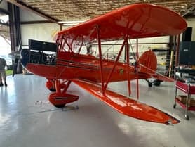 The underside of the front of an orange biplane.