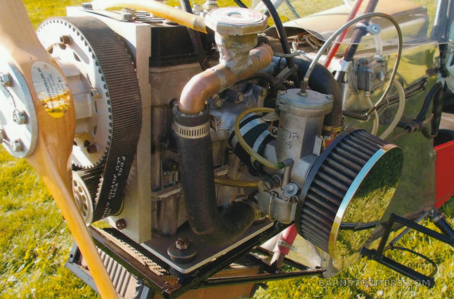 A close-up view of the ultralight aircraft's engine, highlighting the propeller drive belt and carburetor.