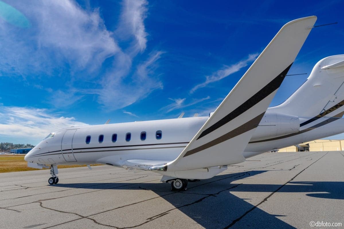 A side view of the white Bombardier Challenger business jet showing the wing and tail with dark grey stripes.