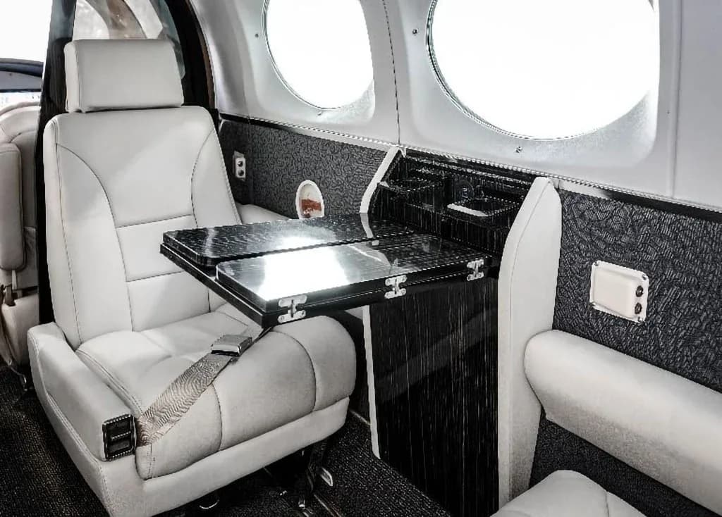 A close-up of a light-colored leather passenger seat with a fold-out table in the aircraft's cabin.