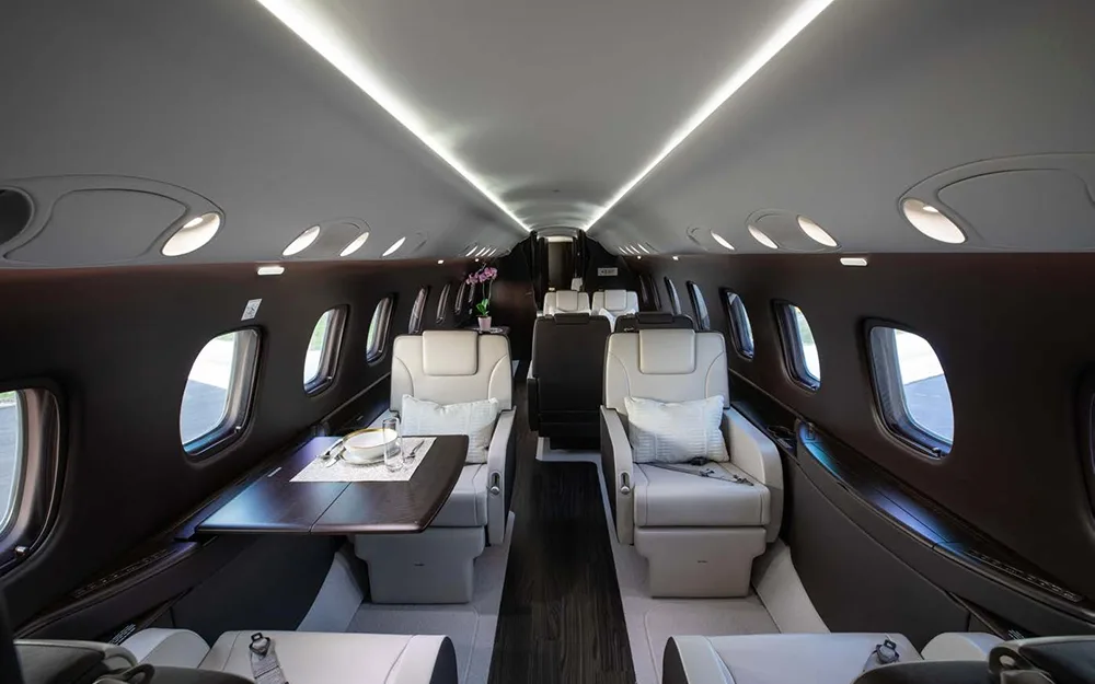 A wide view of the private jet's cabin, showing rows of light-colored seats and a table set for dining.