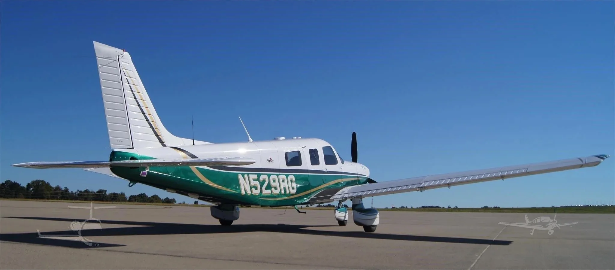 A rear-side view of the white and green Piper 6XT (N529RG) parked on an airfield under a clear blue sky.