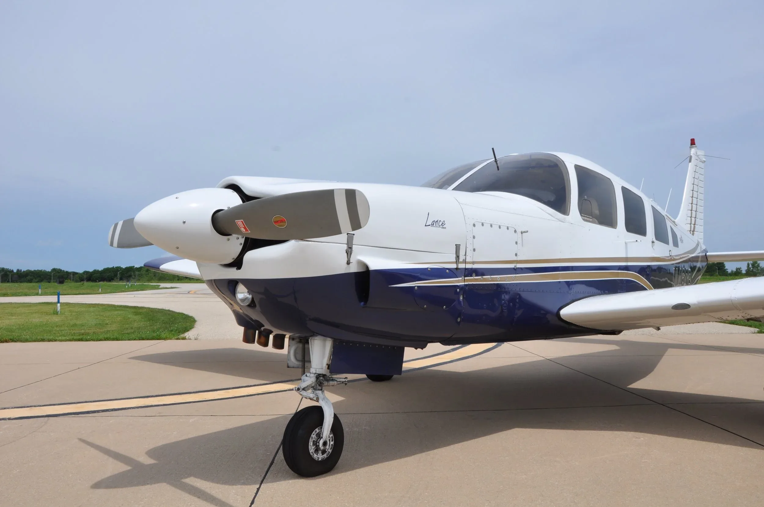 A close-up view of the front of a white and blue Piper Lance aircraft, showing the propeller and nose gear.