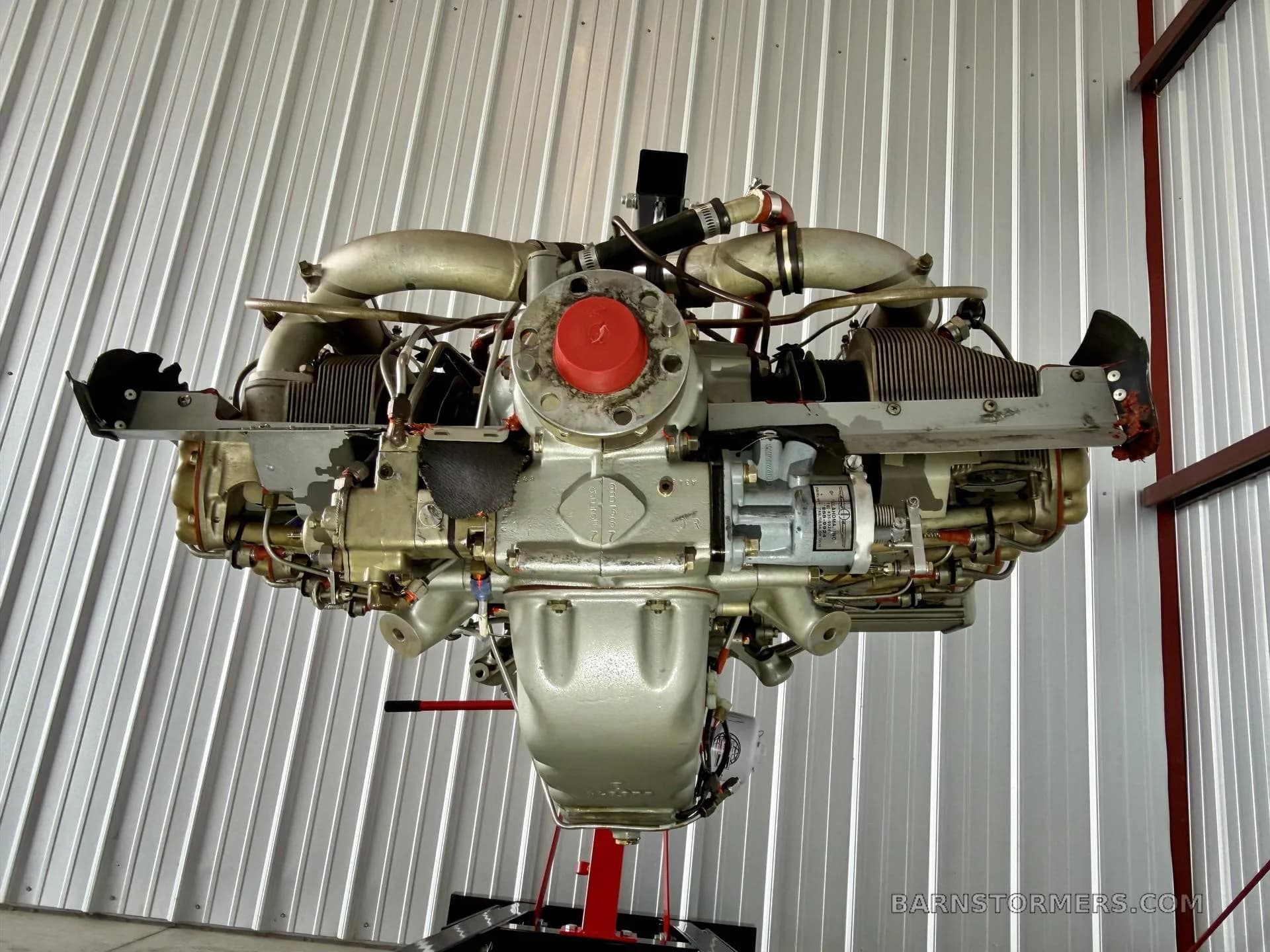 A front view of a Continental aircraft engine, showing the propeller hub area and cylinders, suspended in a hangar.