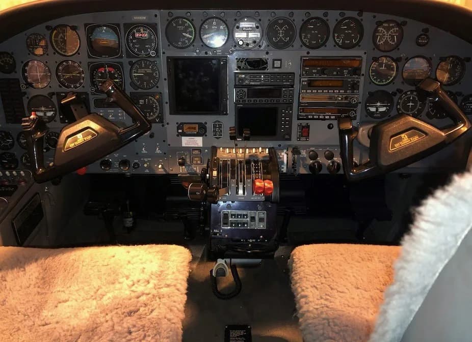 The aircraft's cockpit with a detailed instrument panel, dual yokes, and sheepskin seat covers.