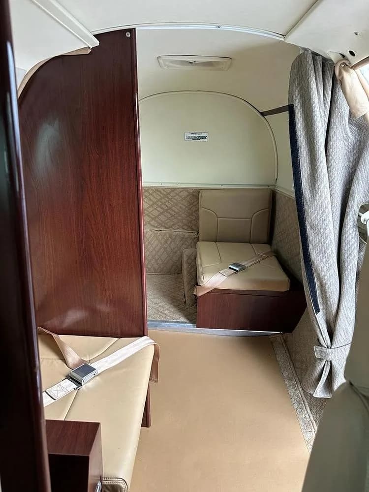 The rear compartment of an aircraft cabin, featuring a tan bench seat and a dark wood partition.
