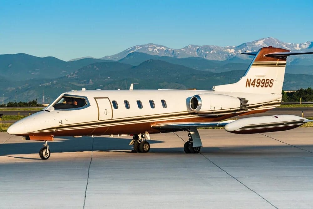 A Learjet 31A with registration N499BS is parked on the tarmac with mountains in the background.
