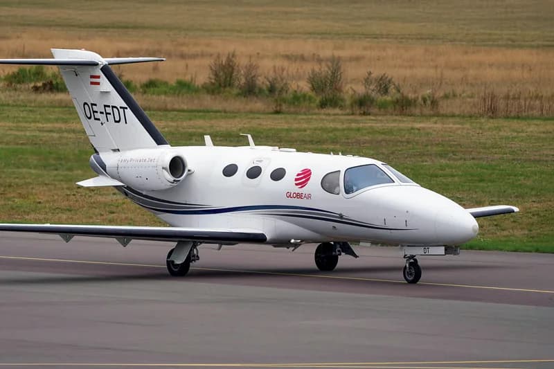 A white GlobeAir Cessna CitationJet (OE-FDT) with blue and grey stripes on a tarmac.