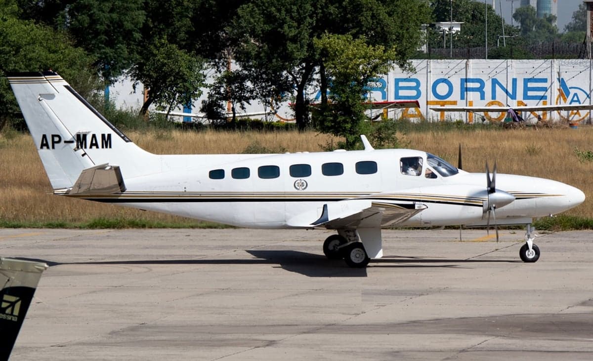 A white twin-engine aircraft with tail number AP-MAM is parked on the tarmac.